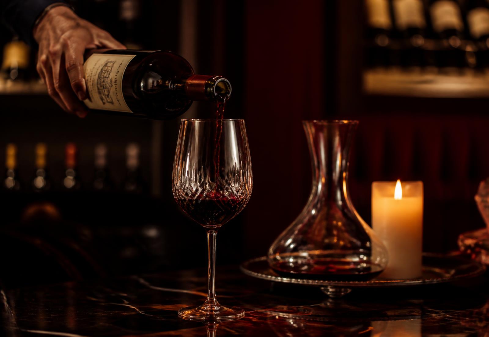 Vin roșu turnat într-un pahar de cristal, la lumina lumânării